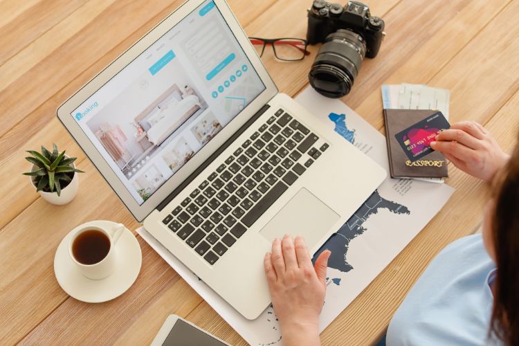 laptop on a desk with a cup of coffee, a camera, passport and an unseen person holding a credit card used on a blog about an integrated payment gateway