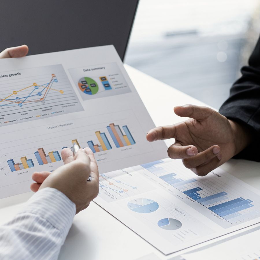 two people's hands pointing at a revenue management chart on a piece of paper with more printed charts on the desk