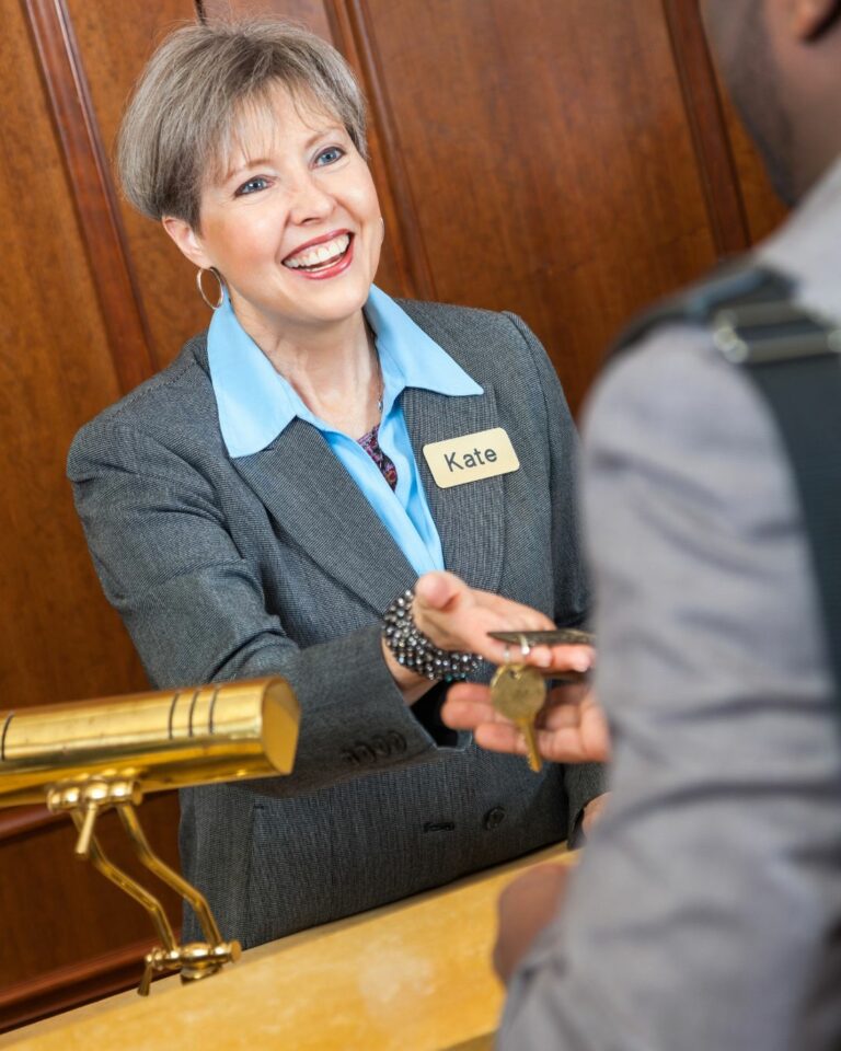smiling female hotel receptionist handing a guest a key used on a blog about guest retention and hotel customer loyalty