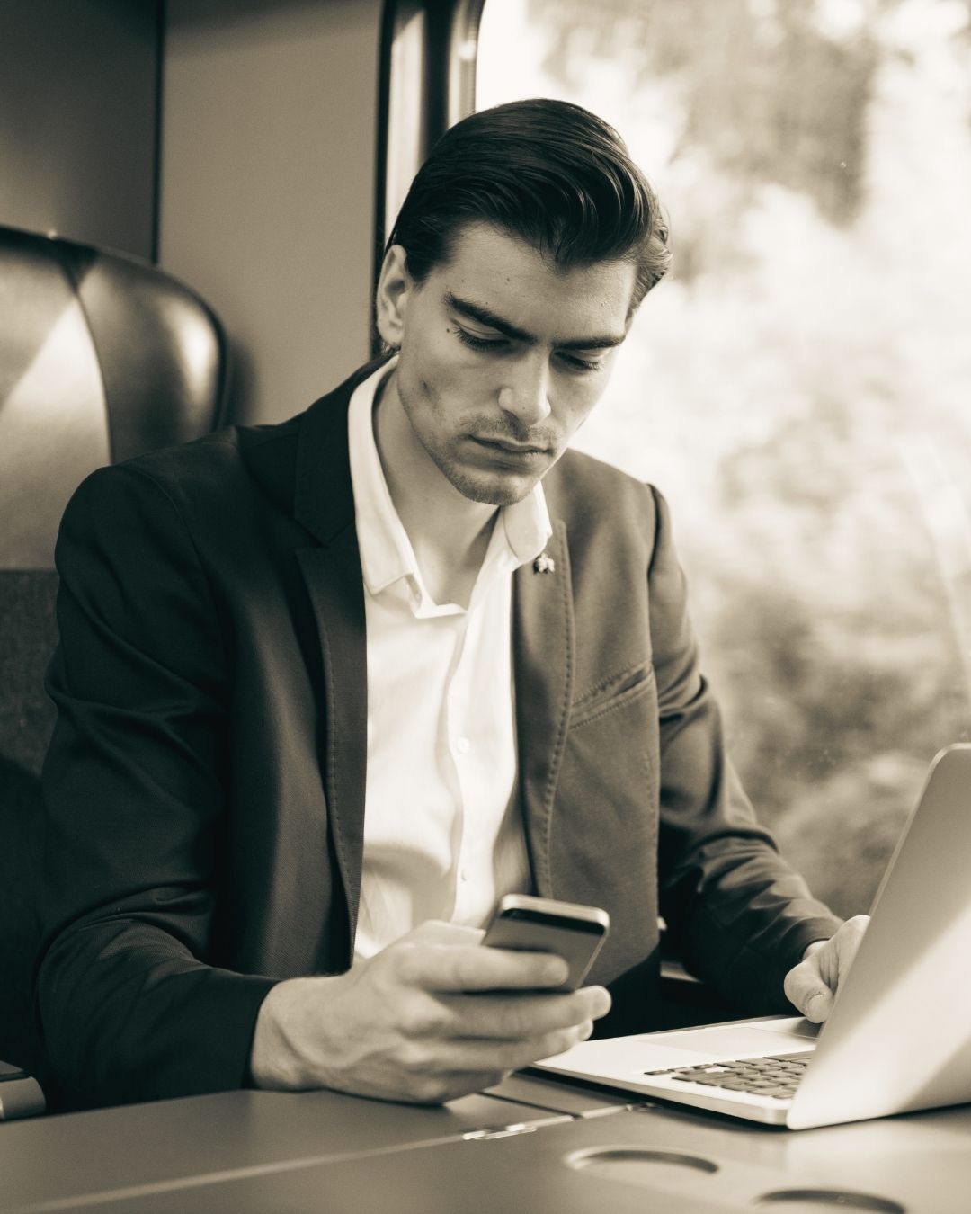 man sitting on a train working on a laptop and looking at his mobile phone used on a blog about cloud based property management software